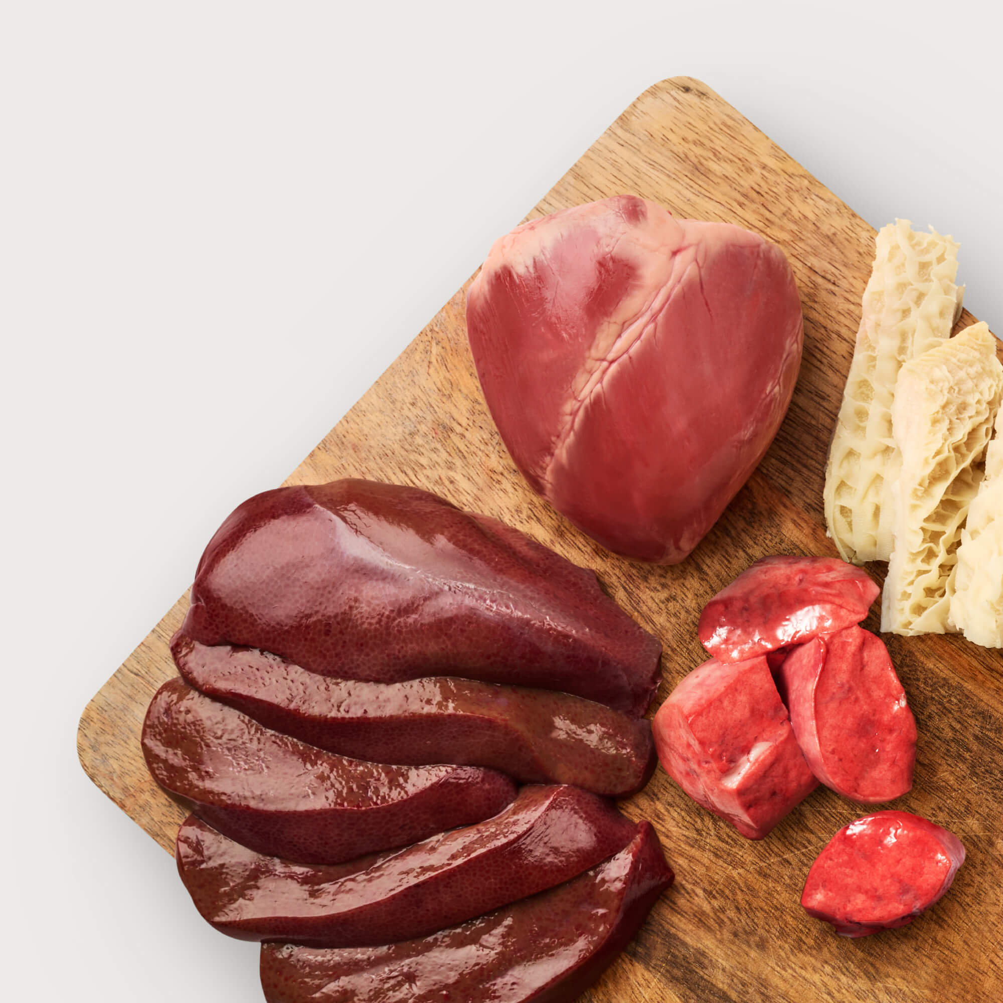 Raw dog food ingredients on wooden cutting board: beef lung, beef, beef liver, beef heart, and beef tripe.