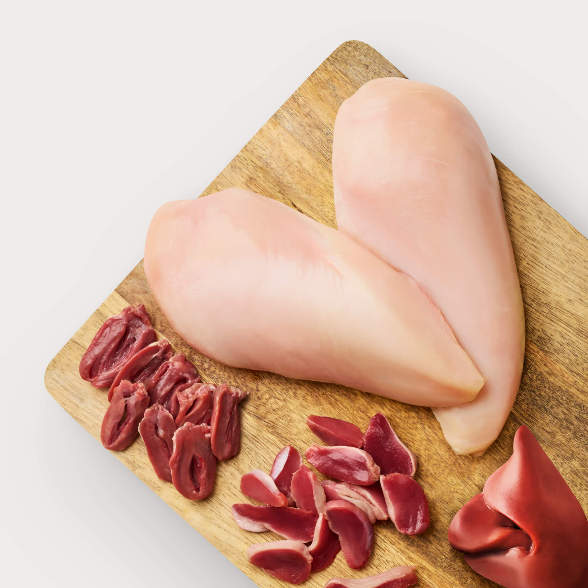 Raw dog food ingredients on wooden cutting board: chicken liver, chicken gizzards, chicken heart, and chicken.